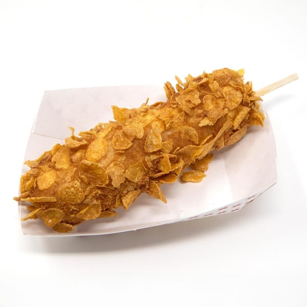 A Daddy Donut corn dog, coated in crispy cereal, rests in a paper tray.