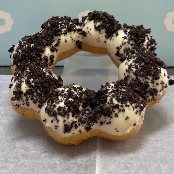 A Daddy Donut mochi donut, white-frosted and covered in dark cookie crumbles, on parchment paper.