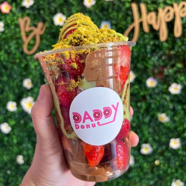 Hand holding a Daddy Donut cup filled with strawberries, chocolate, and pistachio crumble.