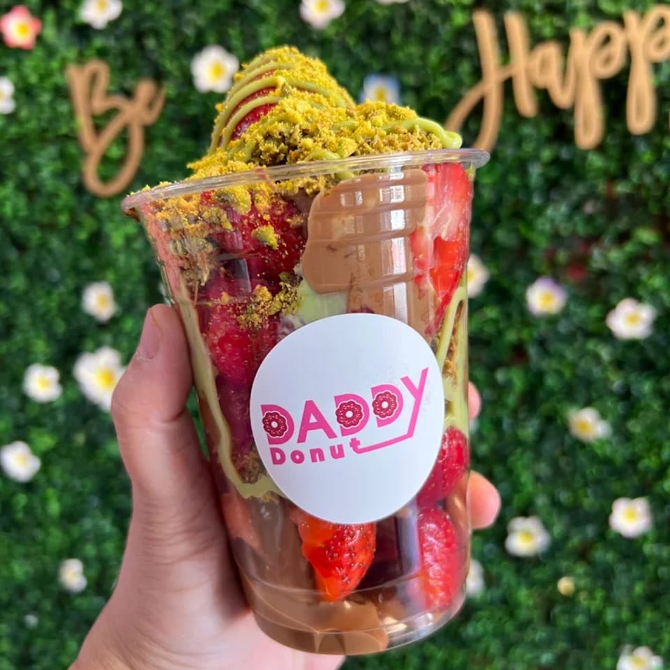 Hand holding a Daddy Donut cup filled with strawberries, chocolate, and pistachio crumble.