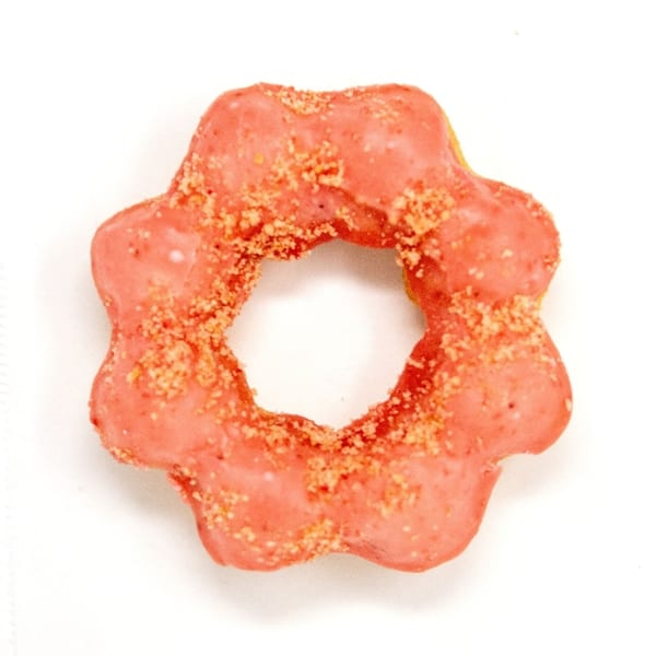 A Daddy Donut mochi donut with pink icing and golden sprinkles on a white background.