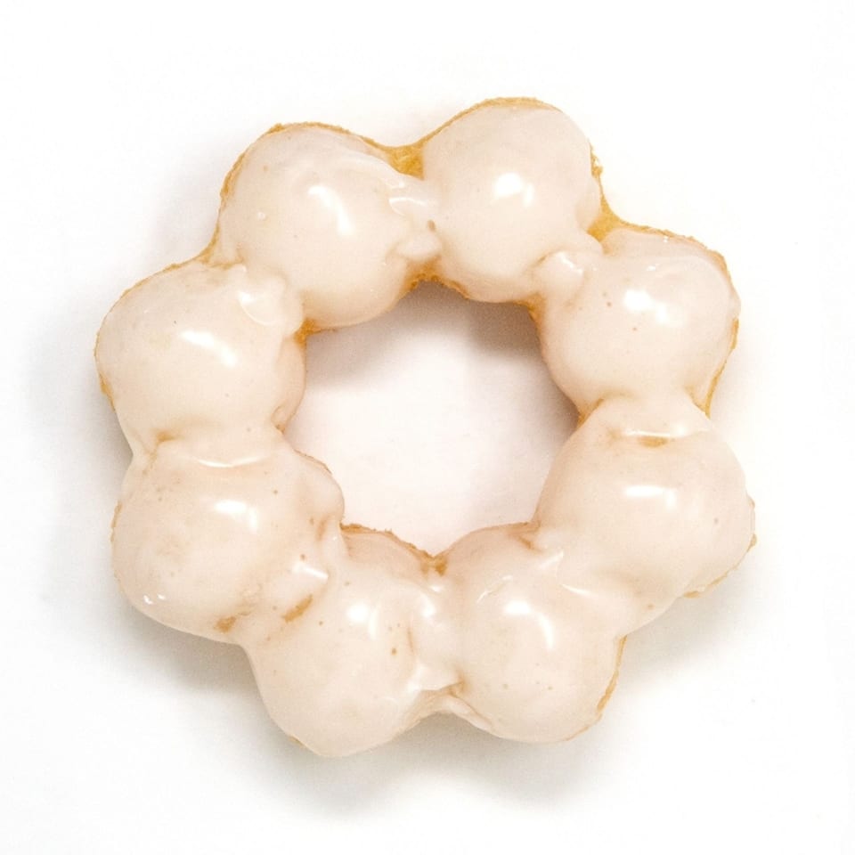 A Daddy Donut mochi donut, light brown with a white glaze, on a white background.