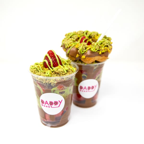 Two Daddy Donut cups with chocolate, strawberries, pistachio crumbles, and a donut on top.
