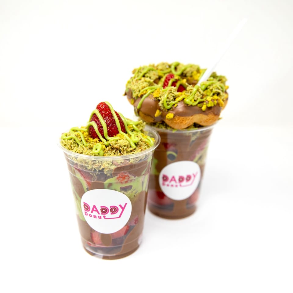 Two Daddy Donut cups with chocolate, strawberries, pistachio crumbles, and a donut on top.